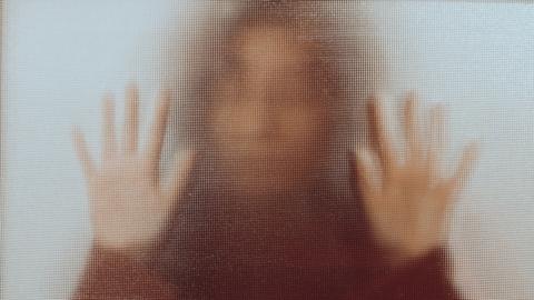 Unrecognisable person standing behind frosted glass