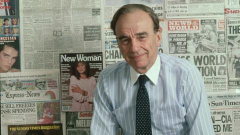 Rupert Murdoch in front of a wall of sample newspapers in 1985
