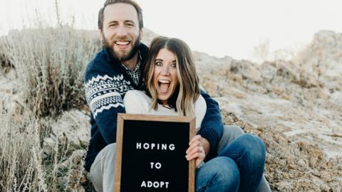 Couple holding sign reading 'Hoping to adopt'