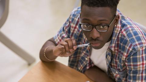 Portrait of male student wearing glasses sitting at desk in classroom - stock photo