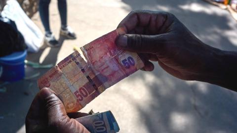 Hands holding a torn 50 rand note