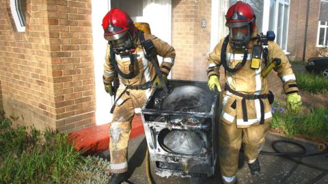 Two firefighters carrying a fire-damaged tumble dryer from a house fire