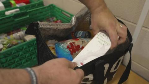 A foodbank volunteer puts a pack of UHT milk into a bag for a foodbank user.