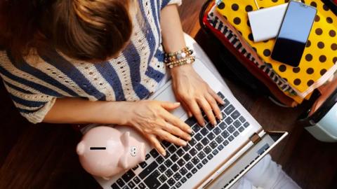 A woman with a piggy bank types on a laptop keyboard