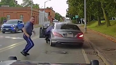A Massachusetts state trooper clings on to car as it suddenly drives away