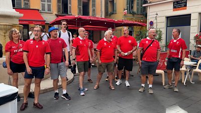 a group of menand women in red shirts singing in front of the street seating at a restaurant in  Nice