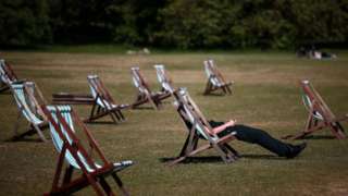A picture of a number of sun loungers on a warm day. A man is sitting in one of them.