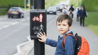 Schoolboy pressing a button at traffic lights on pedestrian crossing on way to school (stock image)