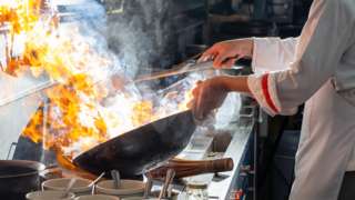 A chef cooks with a flaming wok