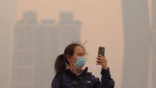 A person wearing a mask uses a cell phone in the hazy conditions