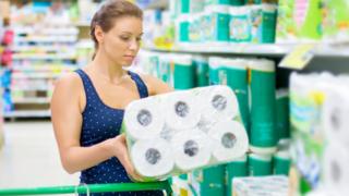 Woman holding toilet paper in supermarket aisle