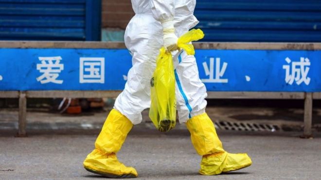 Worker walking past Huanan market with white hazmat suit and yellow boots
