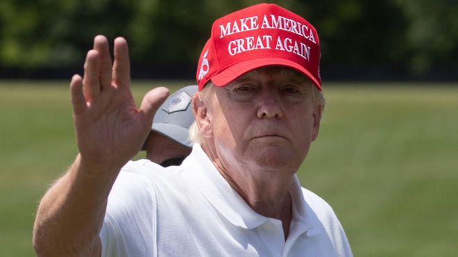 Trump acenando, de boné, em campo de golfe