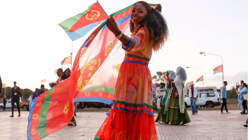 Woman dressed in the colours of the Eritrean flag holding the Eritrean flag.