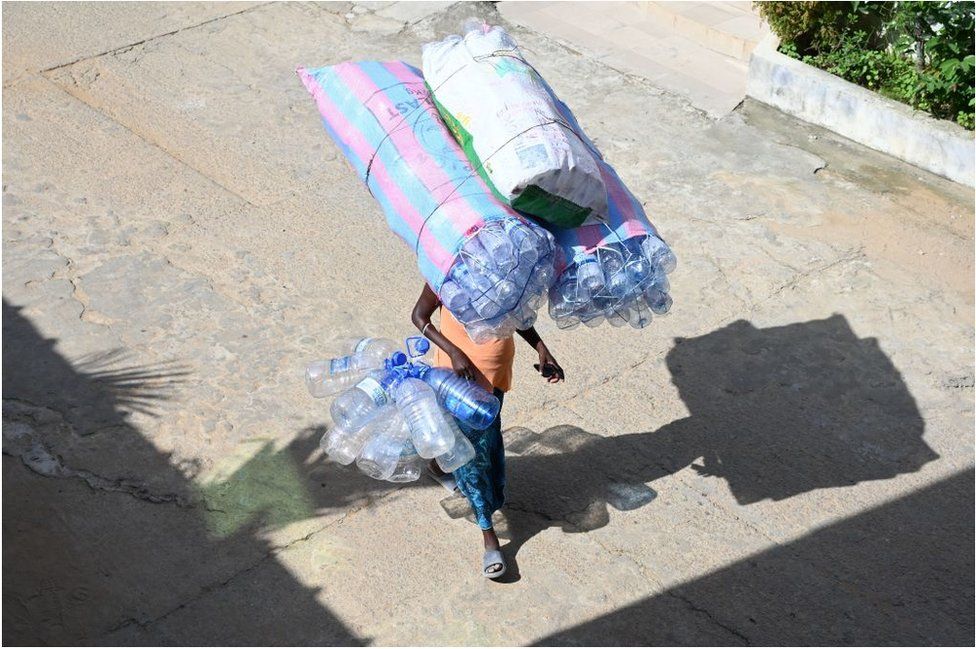 A woman carrying plastic bottles on her head whilst walking down the street.