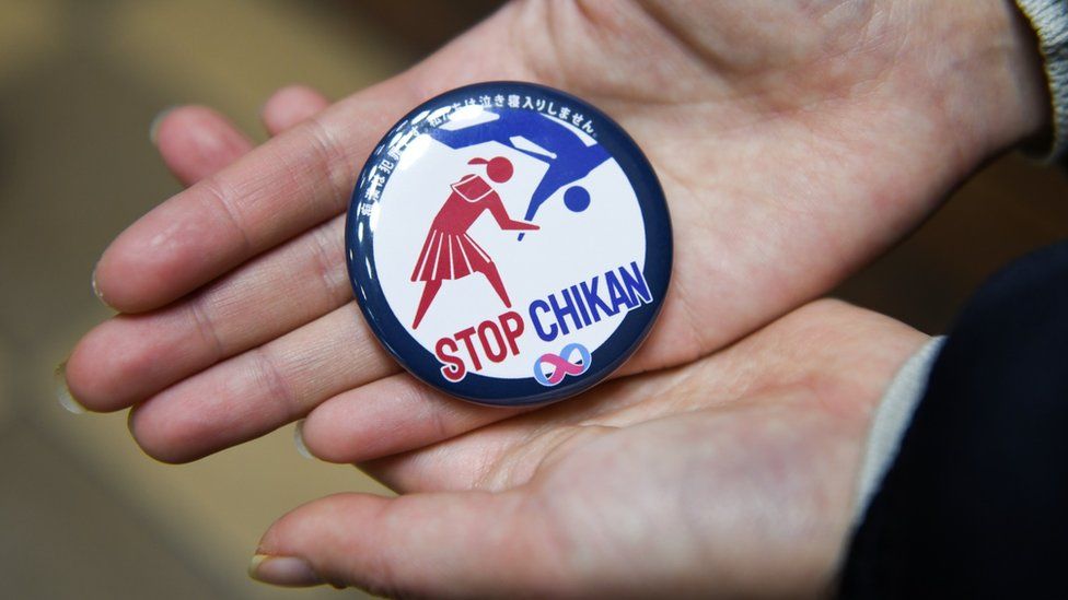 An image of a badge saying "Stop Chikan" with an illustration showing a woman appearing to throw a male attacker to the ground
