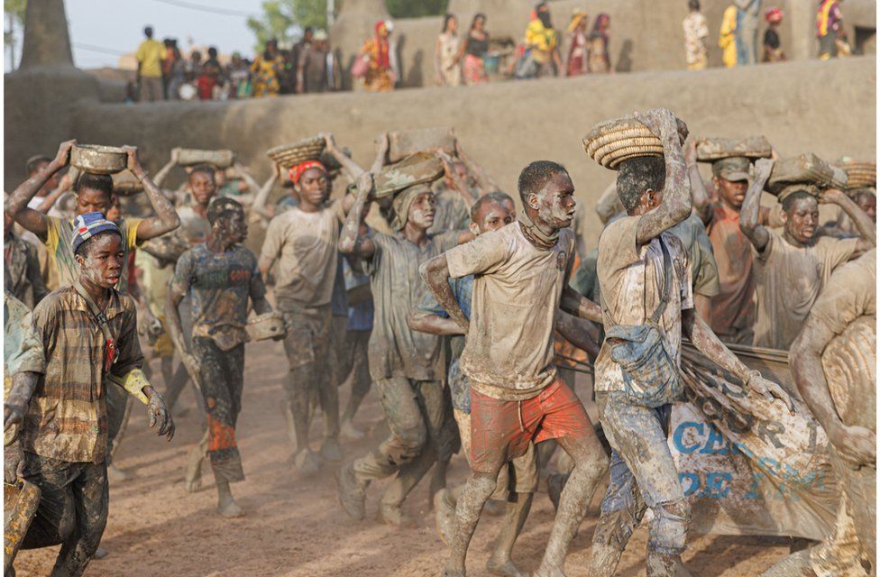 A crowd of people on the move carrying mud buckets - 4 June. They have mud on their bodies.