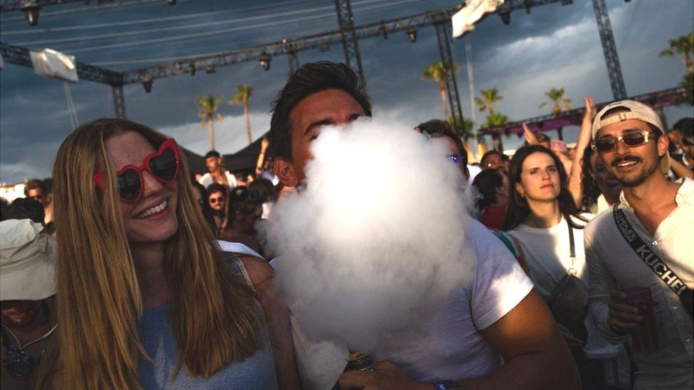 A festival-goer puffs a cloud of smoke from an electronic cigarette standing in a crowd of festival-goers in Cannes, south-eastern France, on 4 August 2023