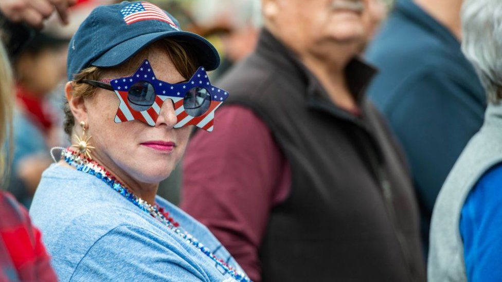 A person wears US Flag glasses while waiting in line at a Make America Great Again Rally with former US President Donald Trump in Manchester, New Hampshire on April 27, 2023.